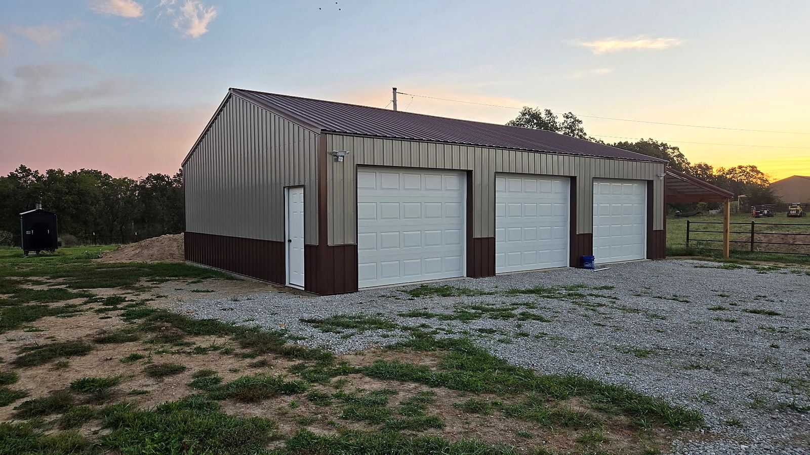 Nichols Construction completed pole barn with three overhead doors at sunset